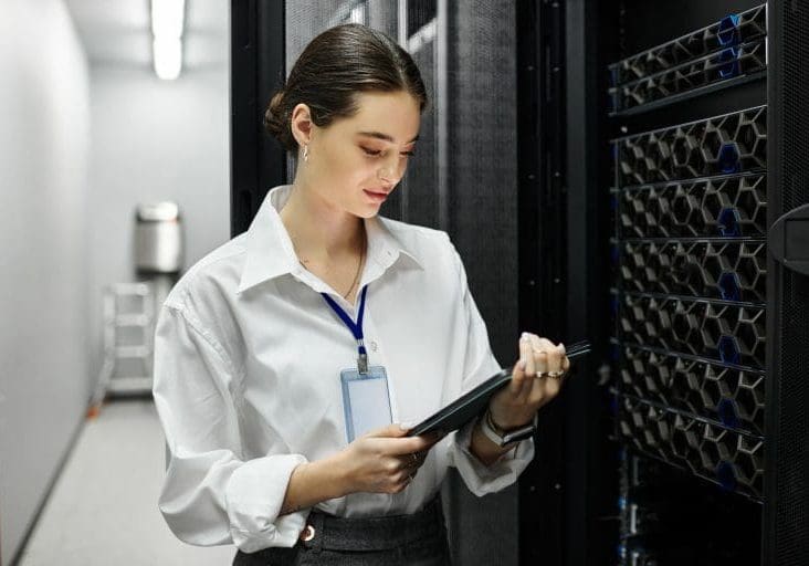 A woman in a white shirt is focused on her tablet while surrounded by server racks.