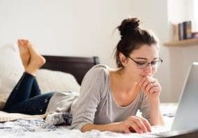Beautiful young woman lying on bed, working. Home office. Beautiful young woman lying on bed, working on notebook, home office.