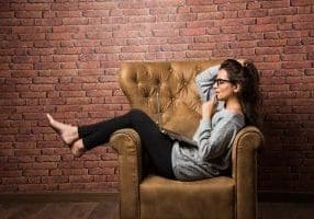 Indian girl with laptop sitting on wing chair against red brick wall Indian girl with laptop sitting on wing chair against red brick wall